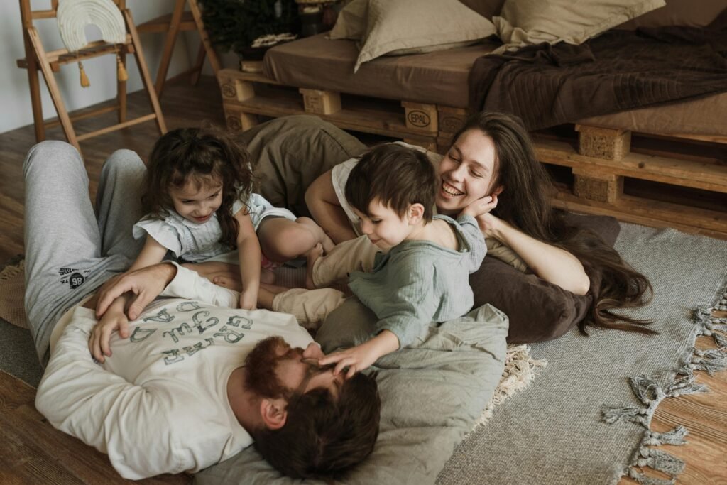 Mother and father sitting on the floor laughing and playing with their two toddlers, sharing a warm and joyful family moment at home