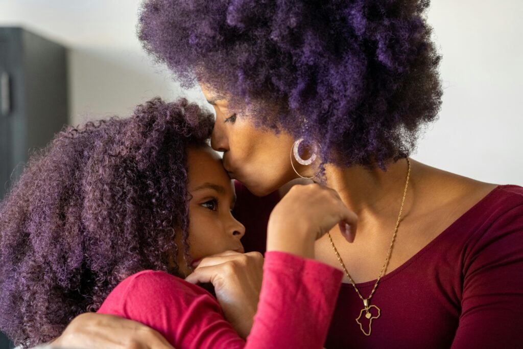 Mother and daughter gently make-up after tantrum Mother gently kissing her child’s forehead while holding them close, offering comfort, warmth, and emotional reassurance during a tender moment.