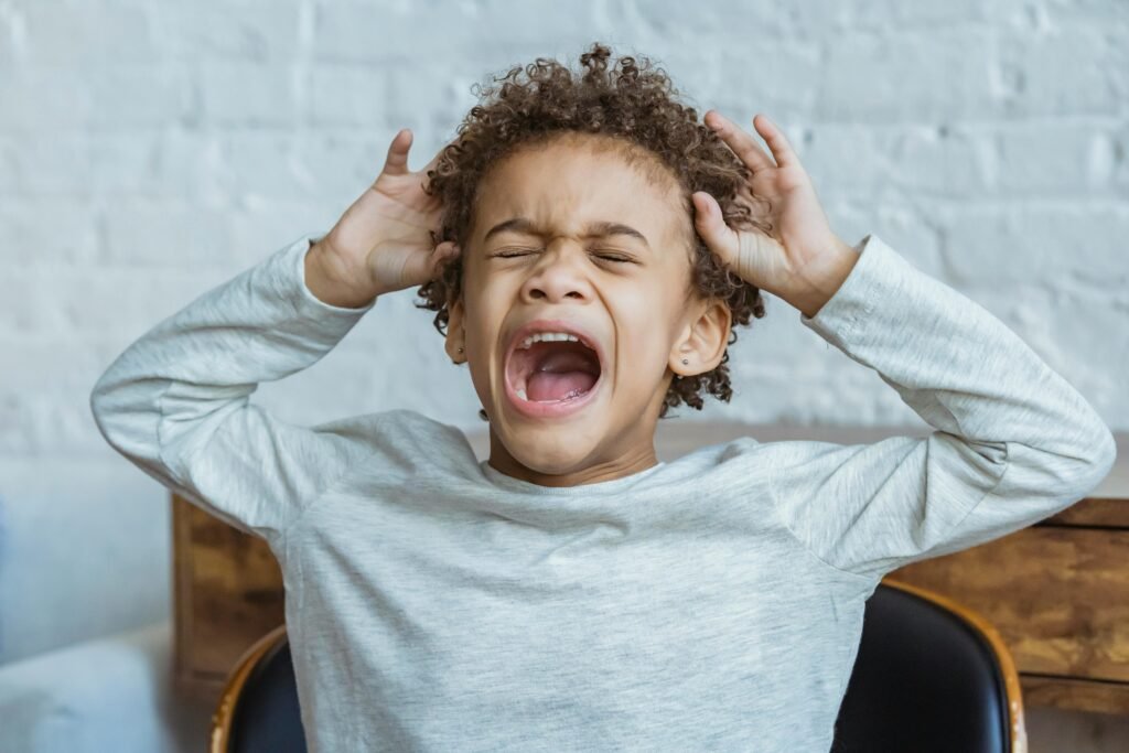 Young boy toddler's tantrum with eyes closed and hands by their head, expressing intense frustration and big emotions