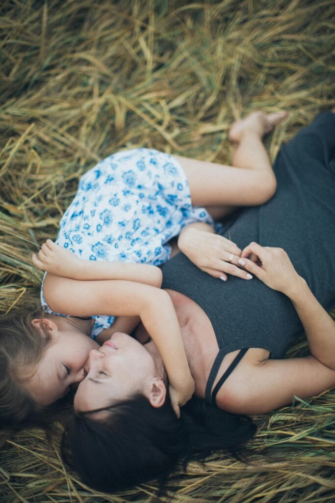 A toddler mom is laying on her back in the grass with her daughter